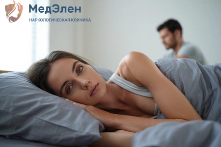 Недовольная девушка ледит на крорвати, сзади нее сидит равнодушный мужчина